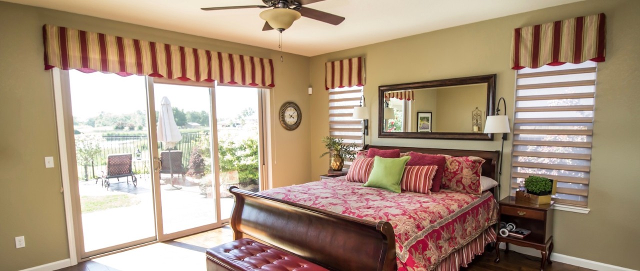 Traditional bedroom with red pattern covers and matching window valance. Shades in the windows.
